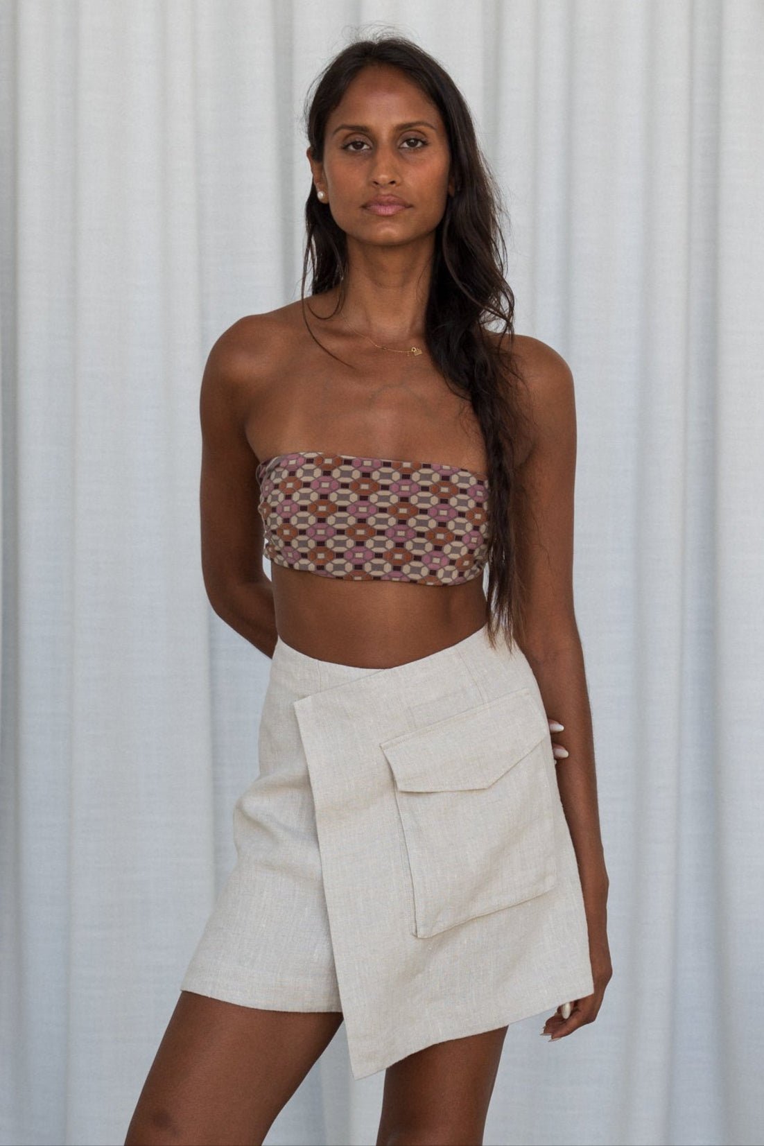 Woman wearing a patterned strapless top and oatmeal Betty linen skirt against a white background