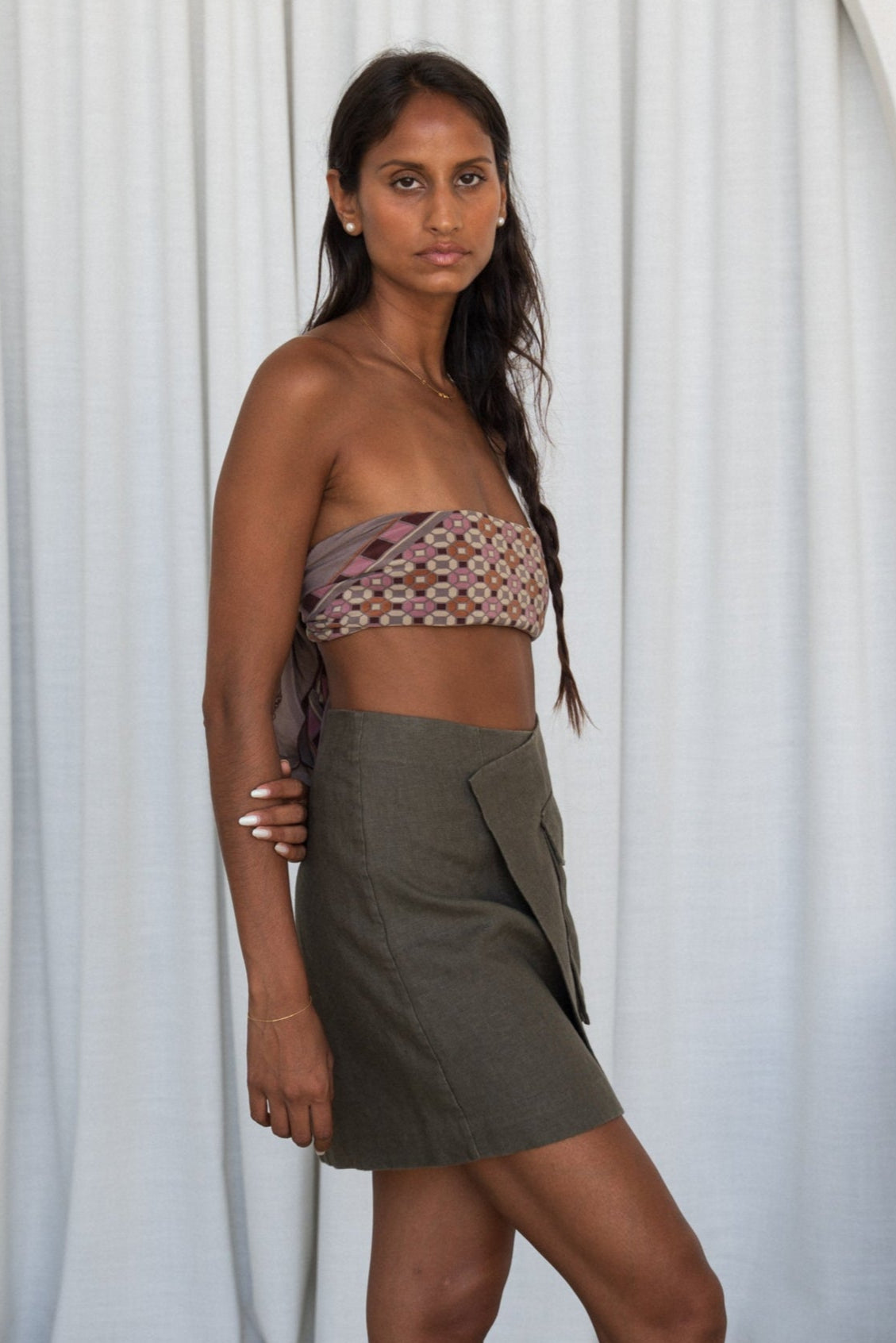 Woman wearing a patterned top and  khaki Betty linen against a white curtain background