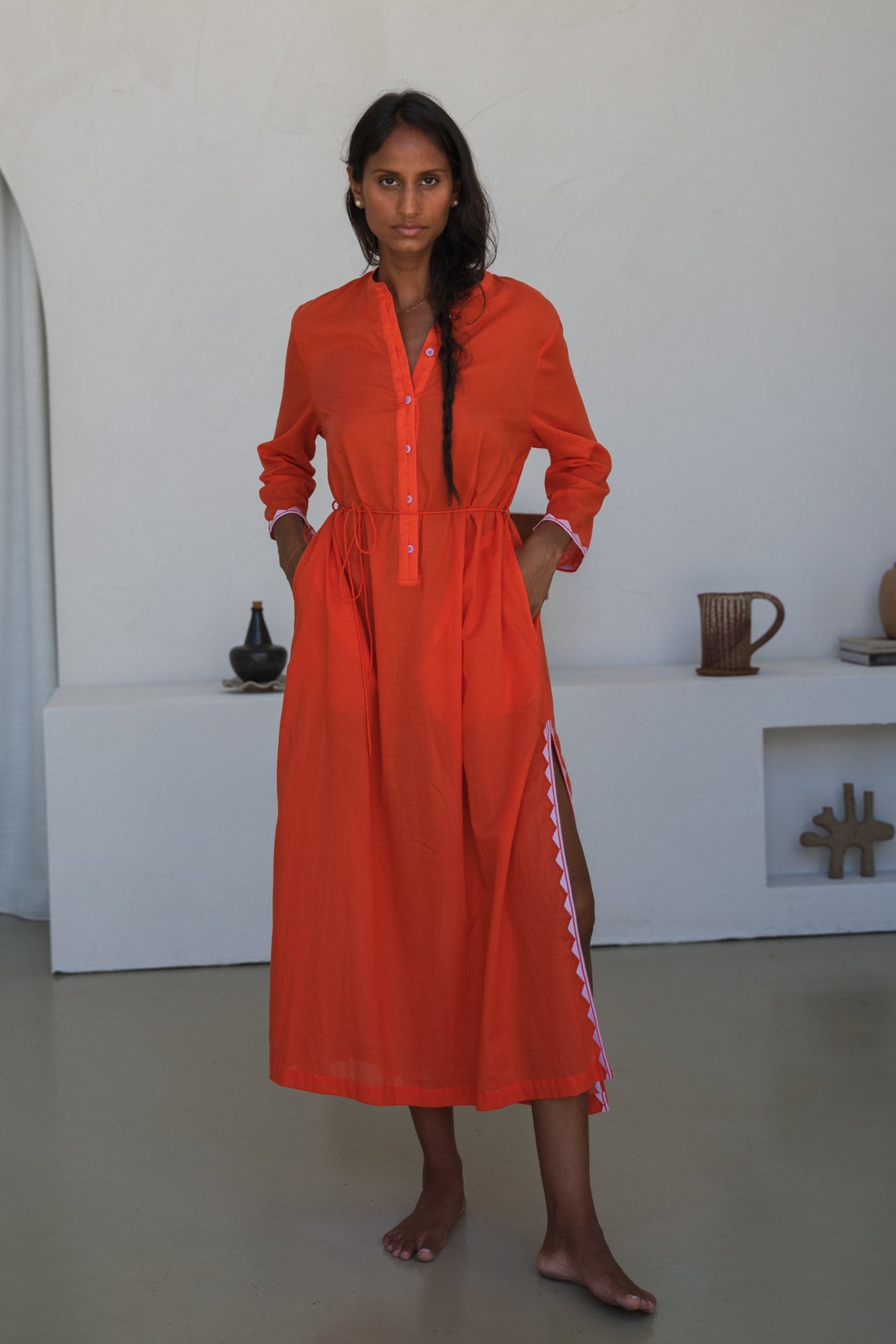 LILLY PILLY woman in a spritz Callie cotton dress standing in a minimalistic room with white walls and a white curtain.