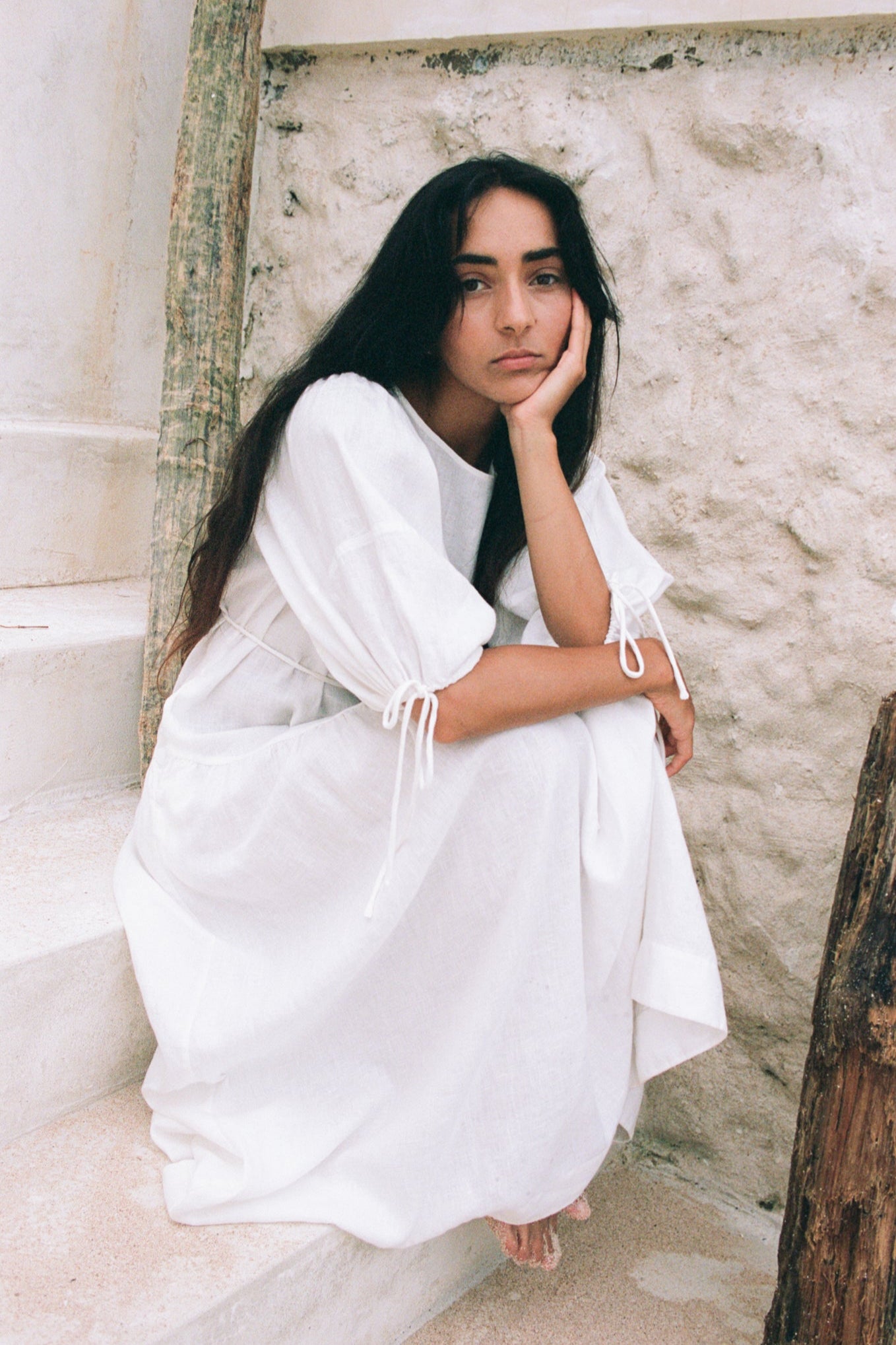 LILLY PILLY woman wearing Charlotte linen dress in Ivory standing by a white textured wall