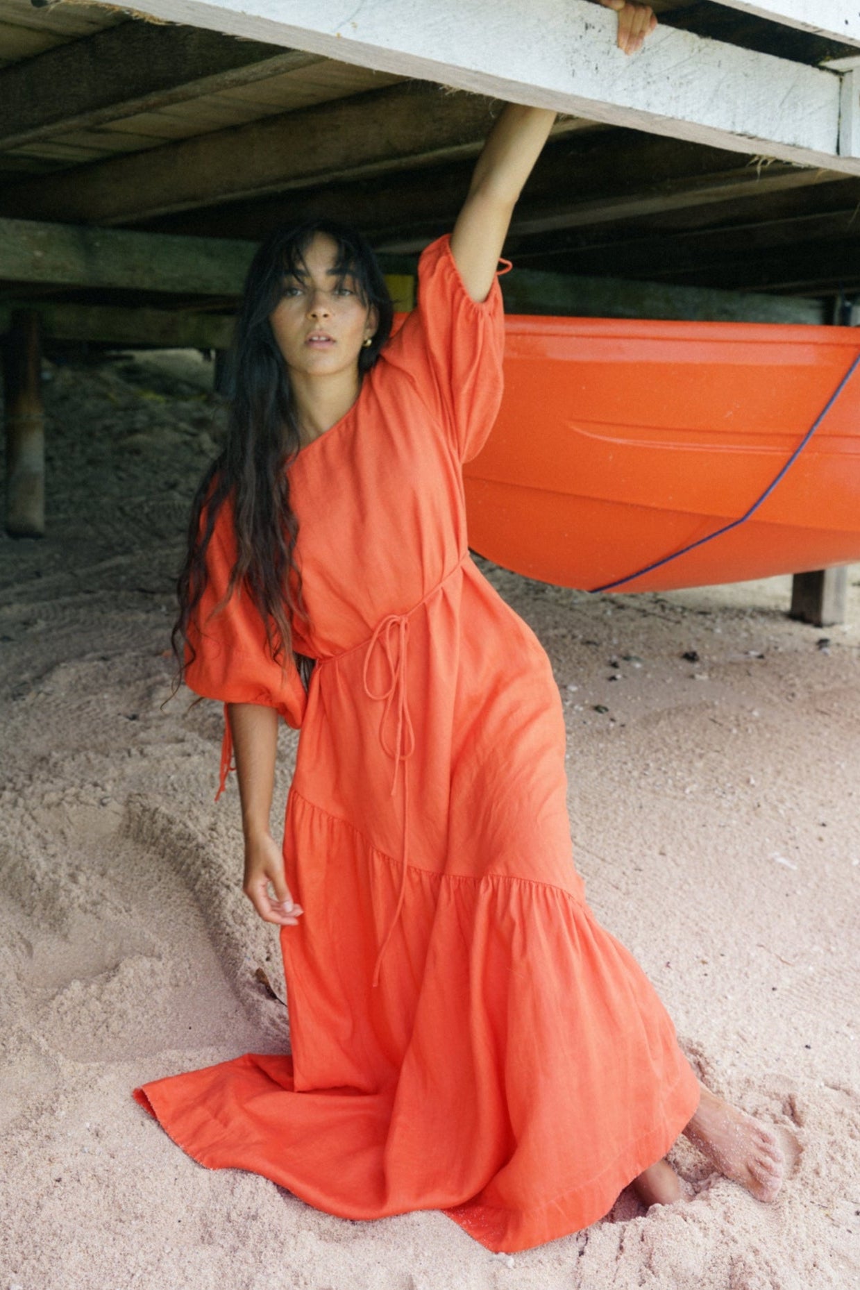 LILLY PILLY woman wearing a spritz coloured Charlotte dress on the sand under a wharf with a boat in the background