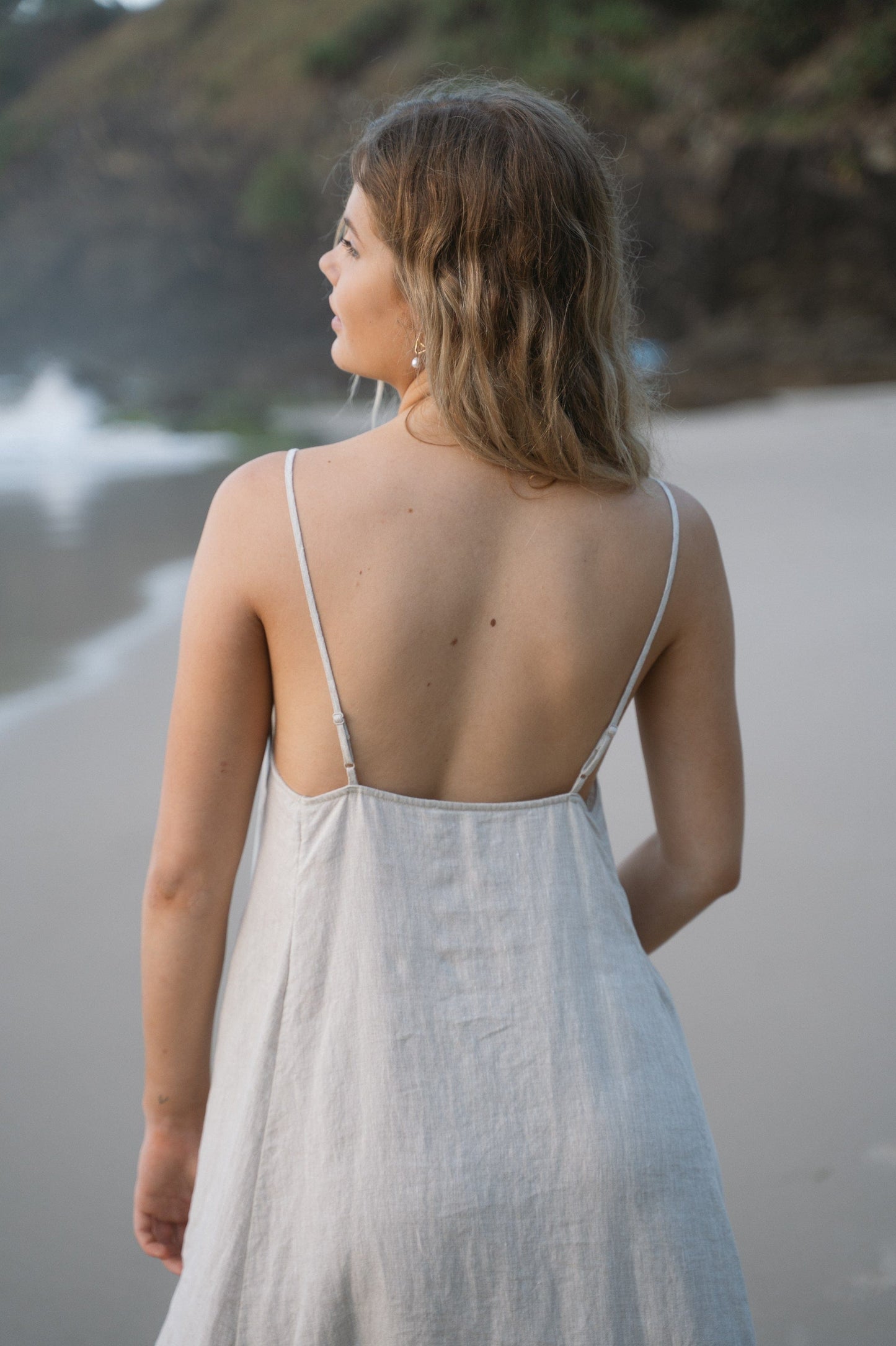 LILLY PILLY woman wearing a oatmeal Coco linen dress showing back view while standing on a beach
