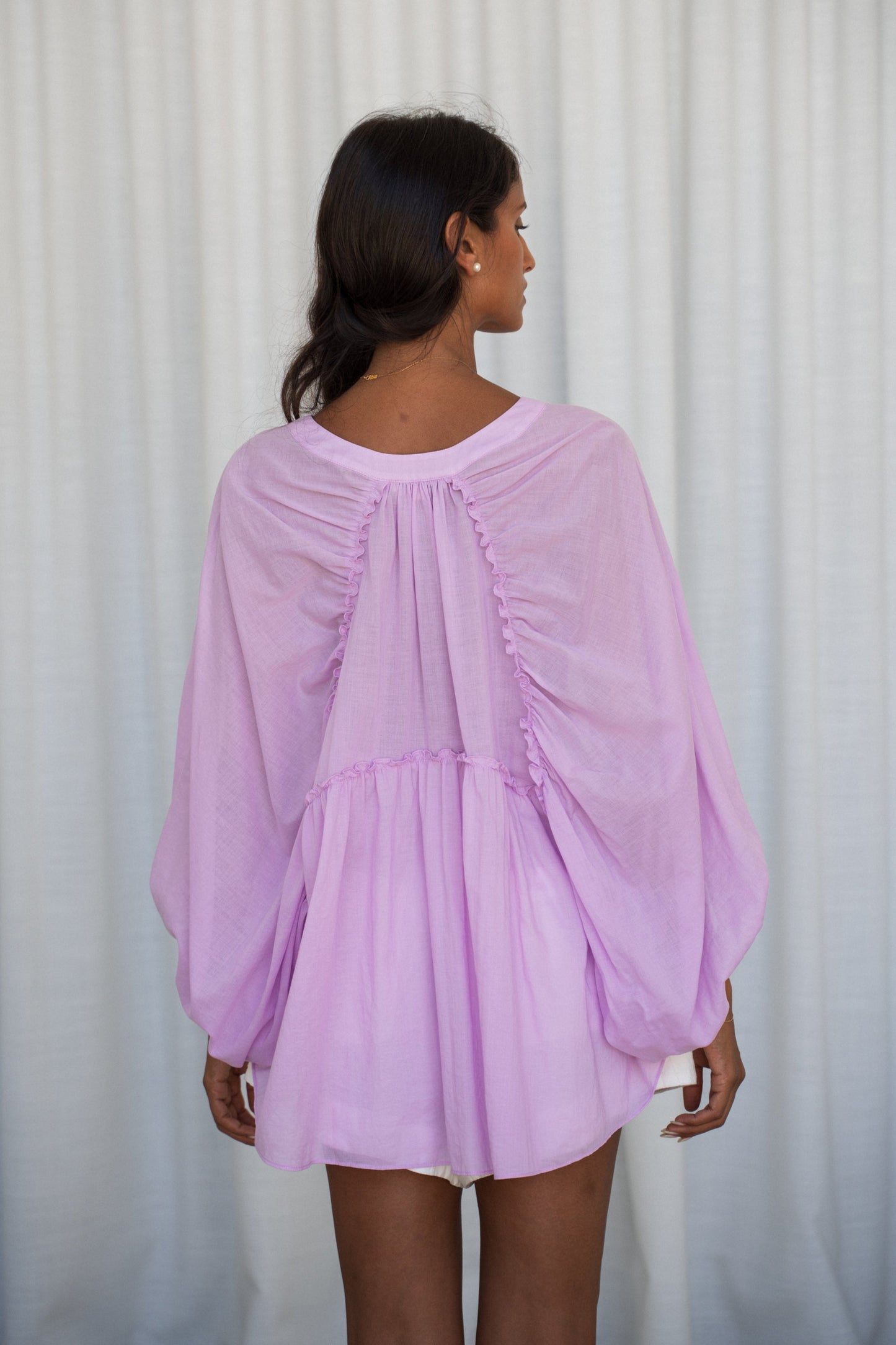 LILLY PILLY woman wearing a orchid Thalia cotton voile shirt  blouse showing back view while standing against a white background