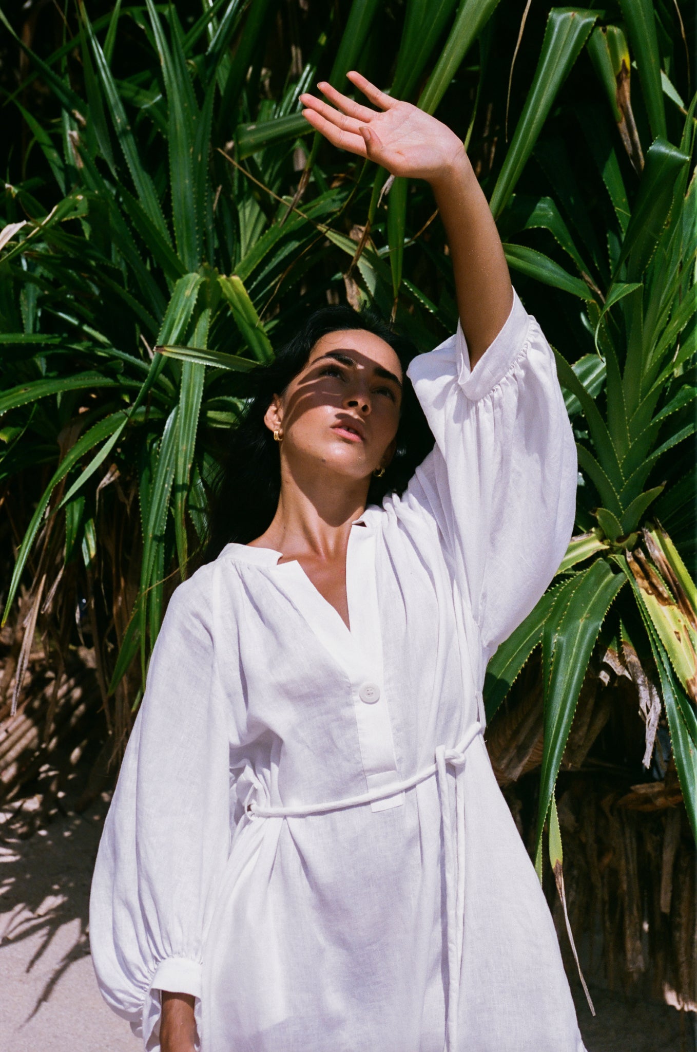 Woman in an ivory Mae linen dress standing in front of green plants