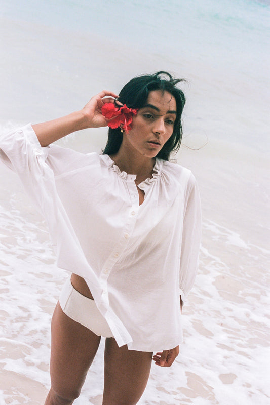 LILLY PILLY woman wearing a ivory Thalia cotton voile shirt blouse with a flower in her hair standing by the waters edge