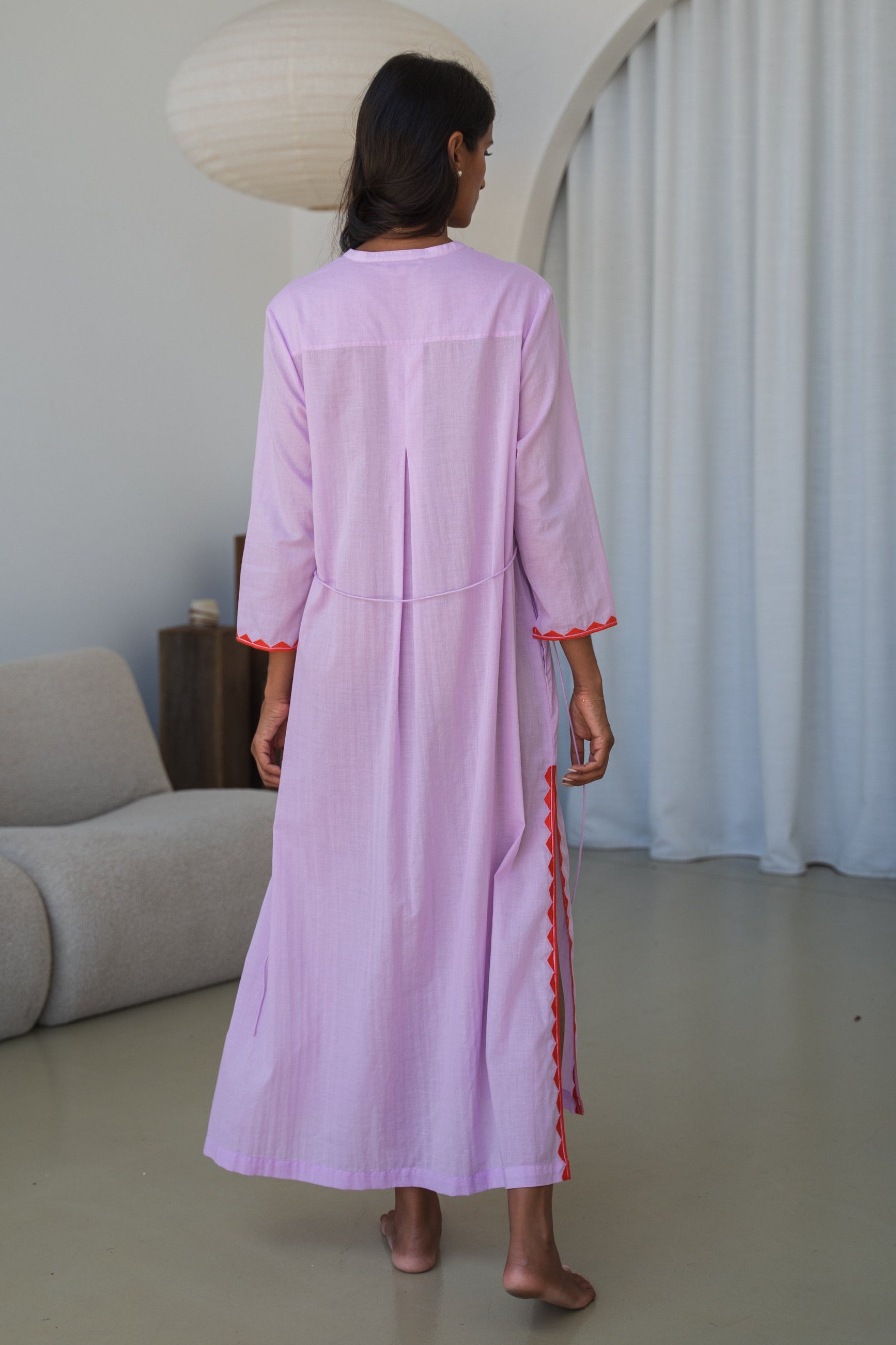 LILLY PILLY woman in a orchid Callie cotton dress standing in a minimalistic room showing back view