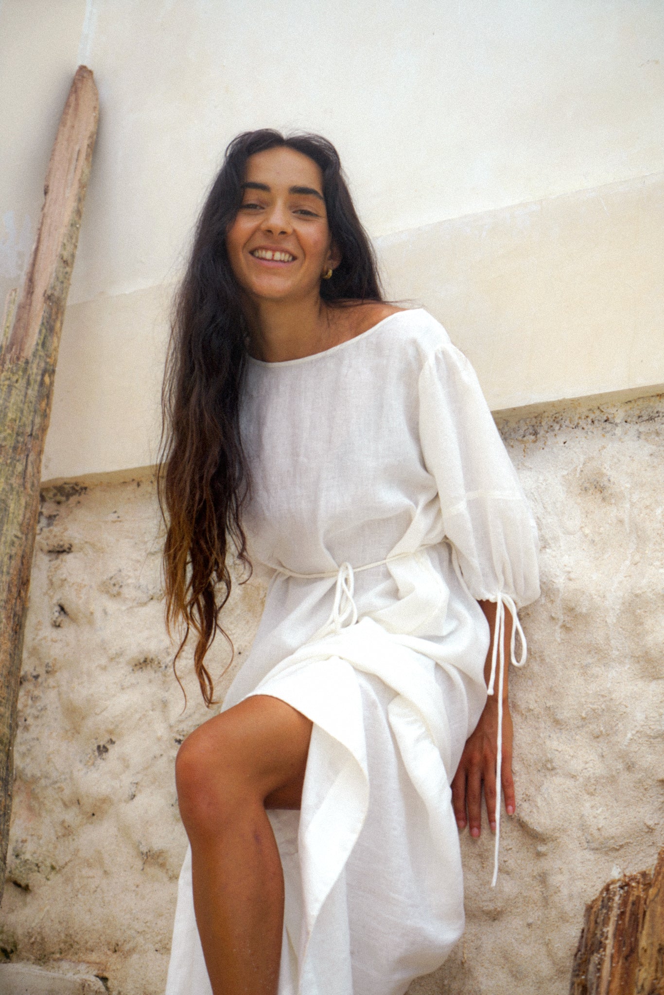 LILLY PILLY woman wearing Charlotte linen dress in Ivory standing by a white textured wall