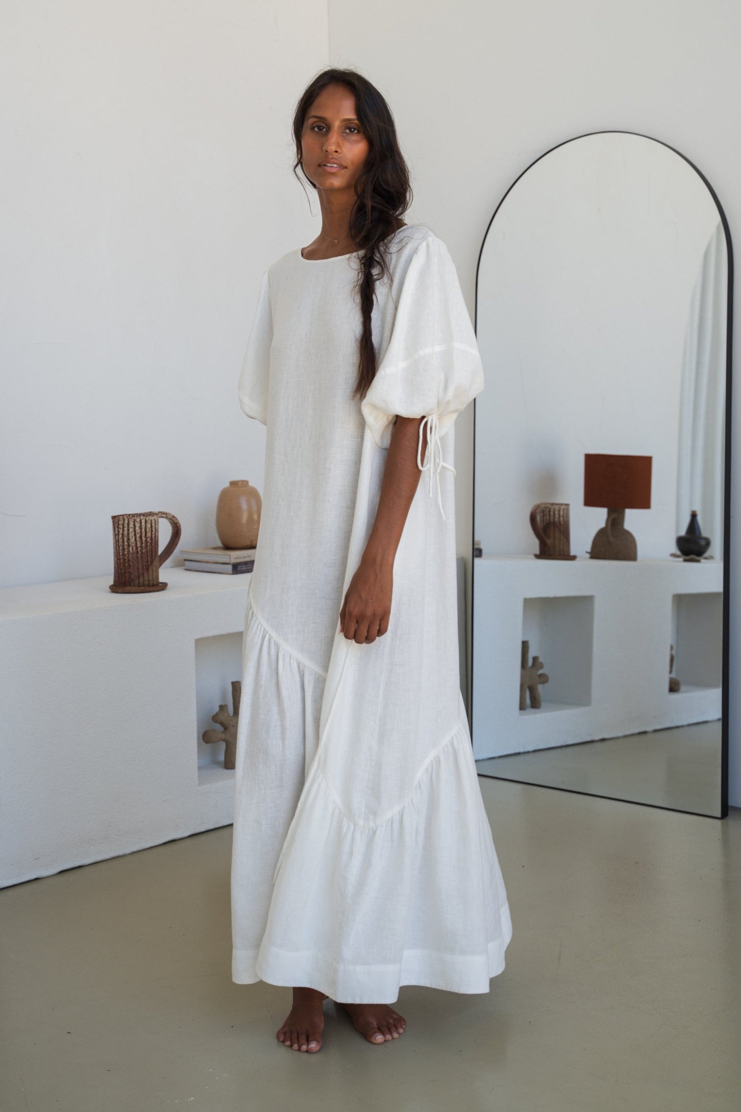 LILLY PILLY woman wearing Charlotte linen dress in Ivory standing by a mirror