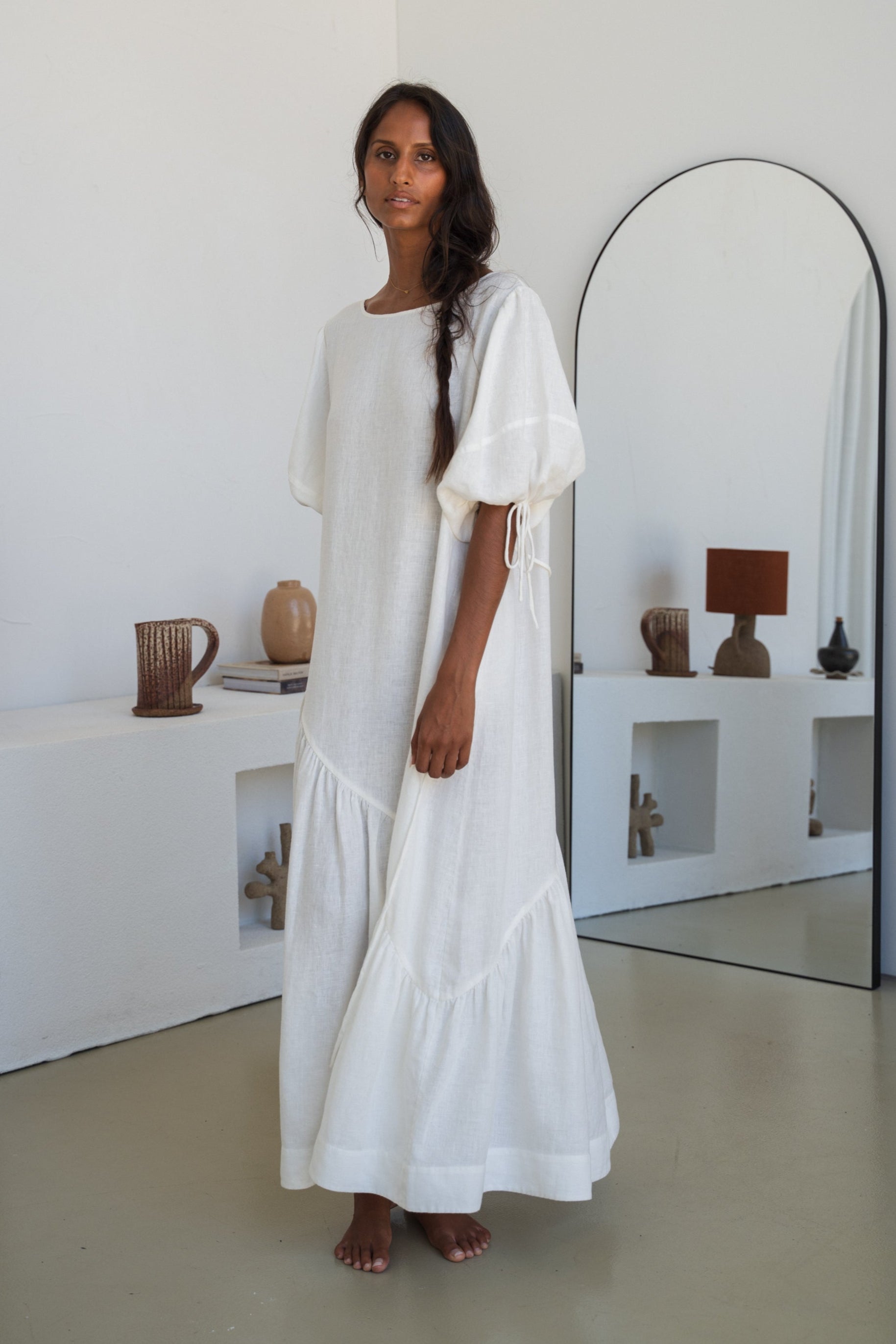LILLY PILLY woman wearing Charlotte linen dress in Ivory standing by a mirror