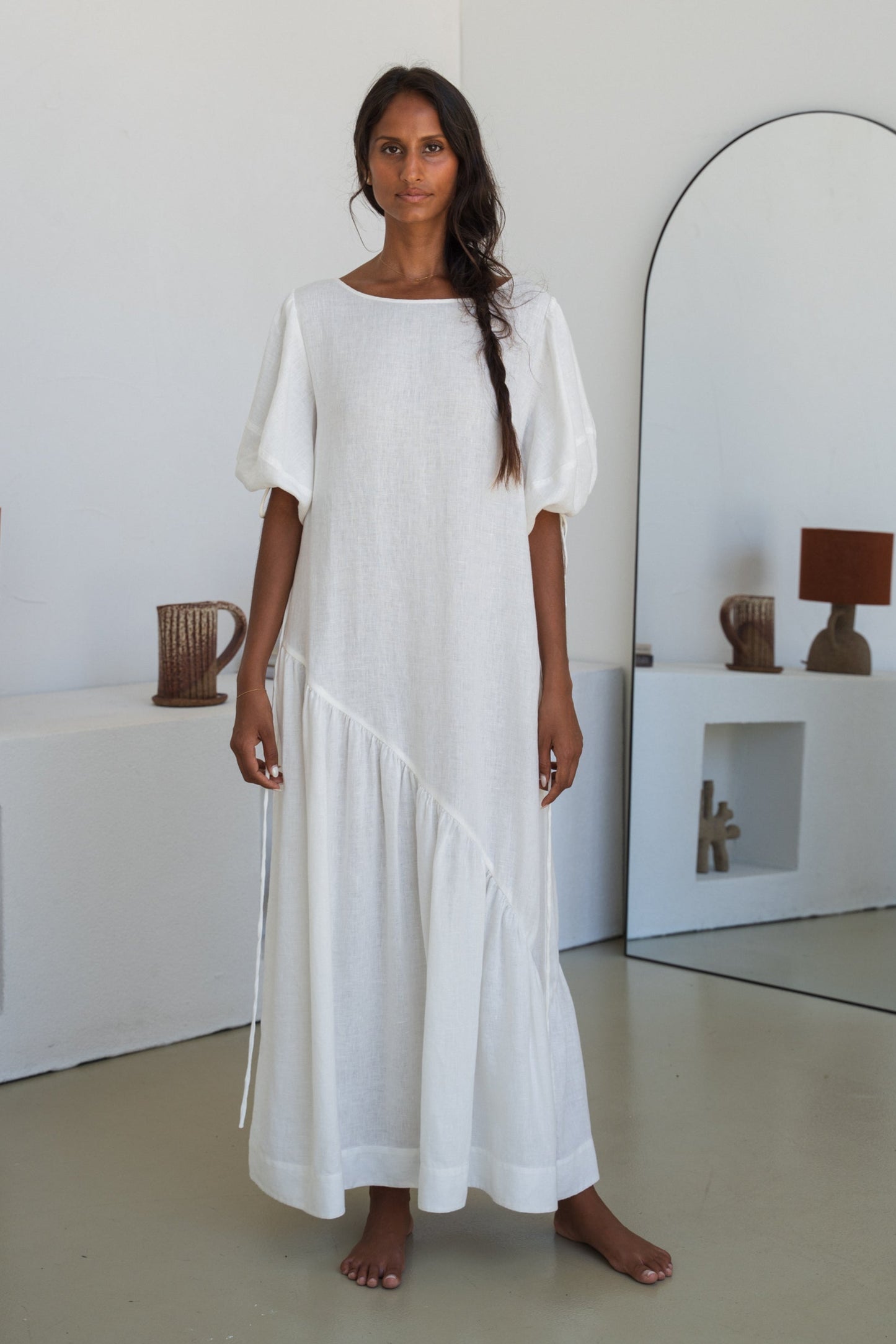 LILLY PILLY woman wearing Charlotte linen dress in Ivory standing by a mirror