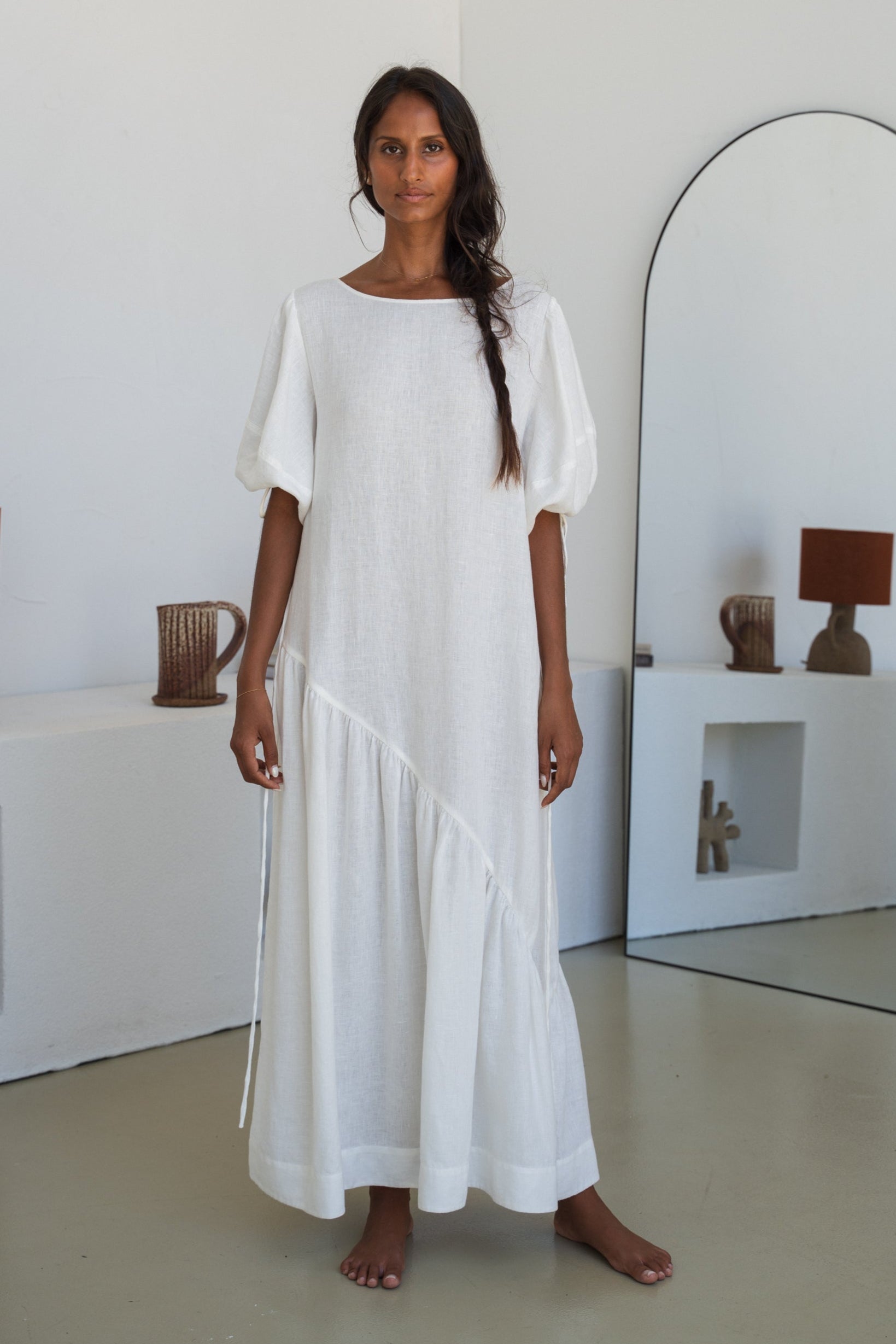 LILLY PILLY woman wearing Charlotte linen dress in Ivory standing by a mirror