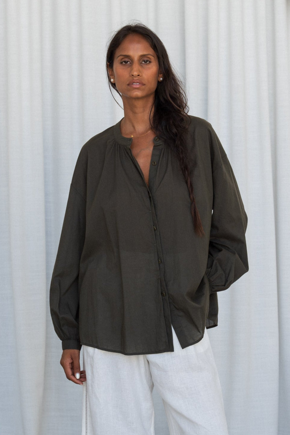 LILLY PILLY woman wearing a khaki Ember cotton voile shirt and ivory linen pants against a light curtain background