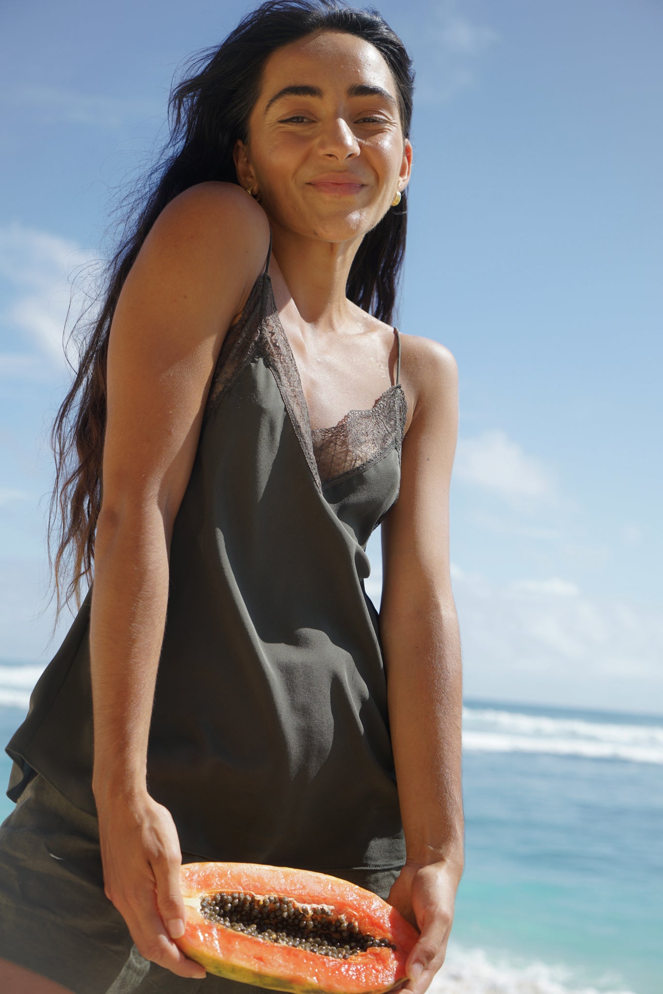 LILLY PILLY woman wearing Frankie silk cami in khaki with papaya by the ocean with a clear blue sky.