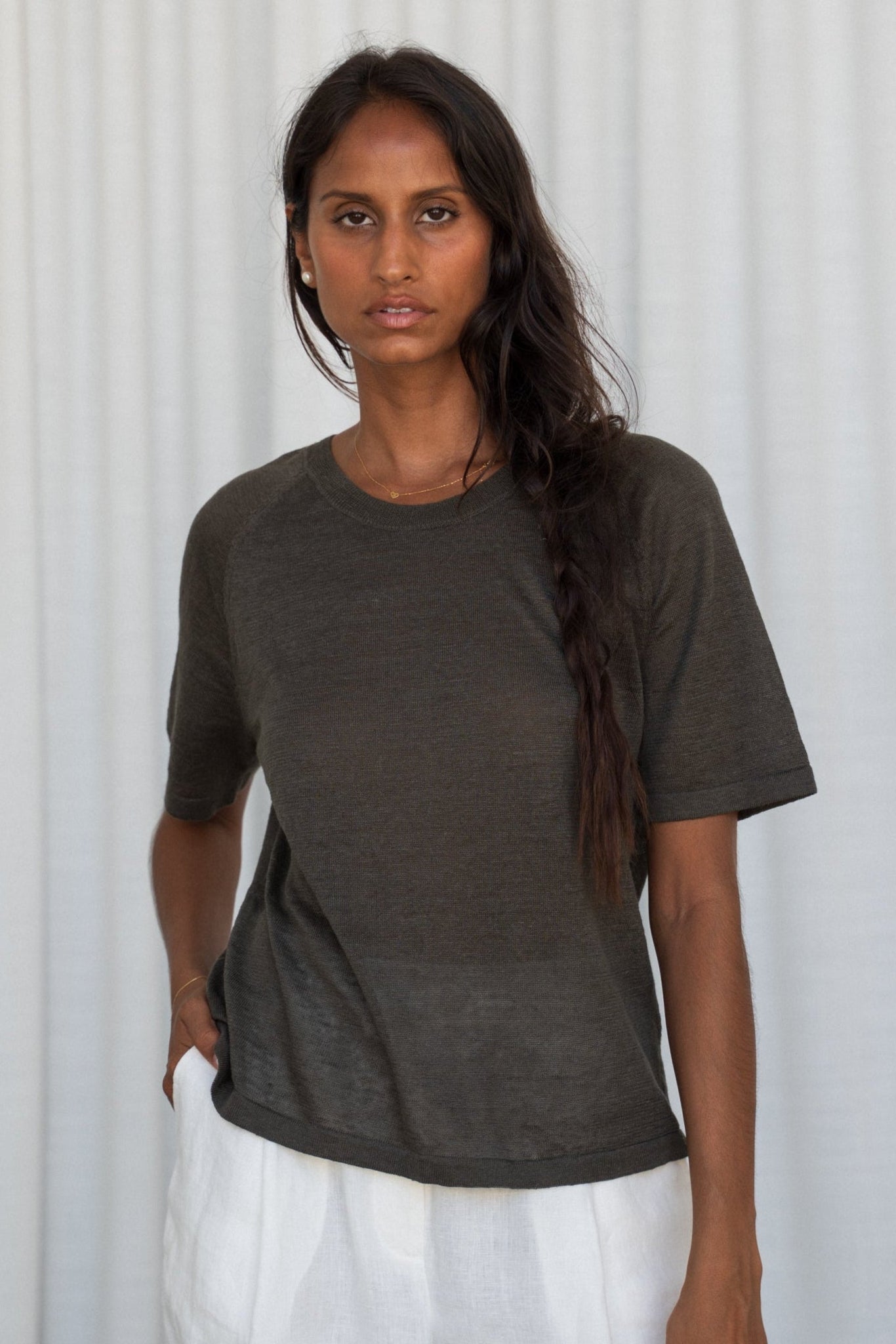 Woman wearing a khaki Grace linen knit top front view with white curtain wall background
