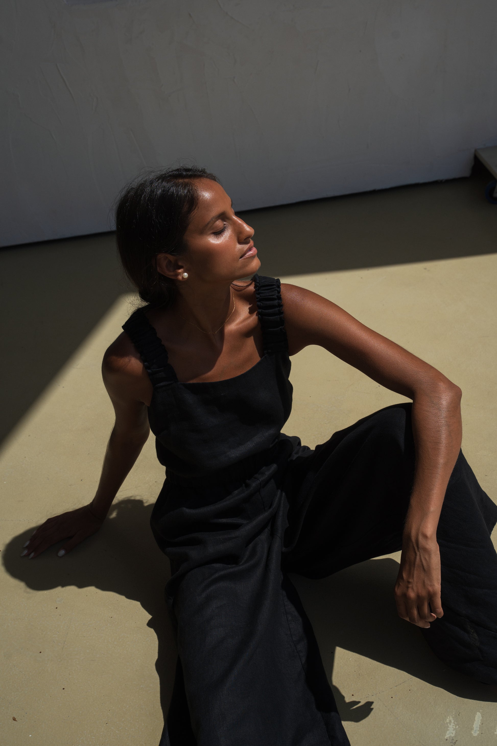 LILLY PILLY woman wearing a black Keely linen jumpsuit sitting in the sun