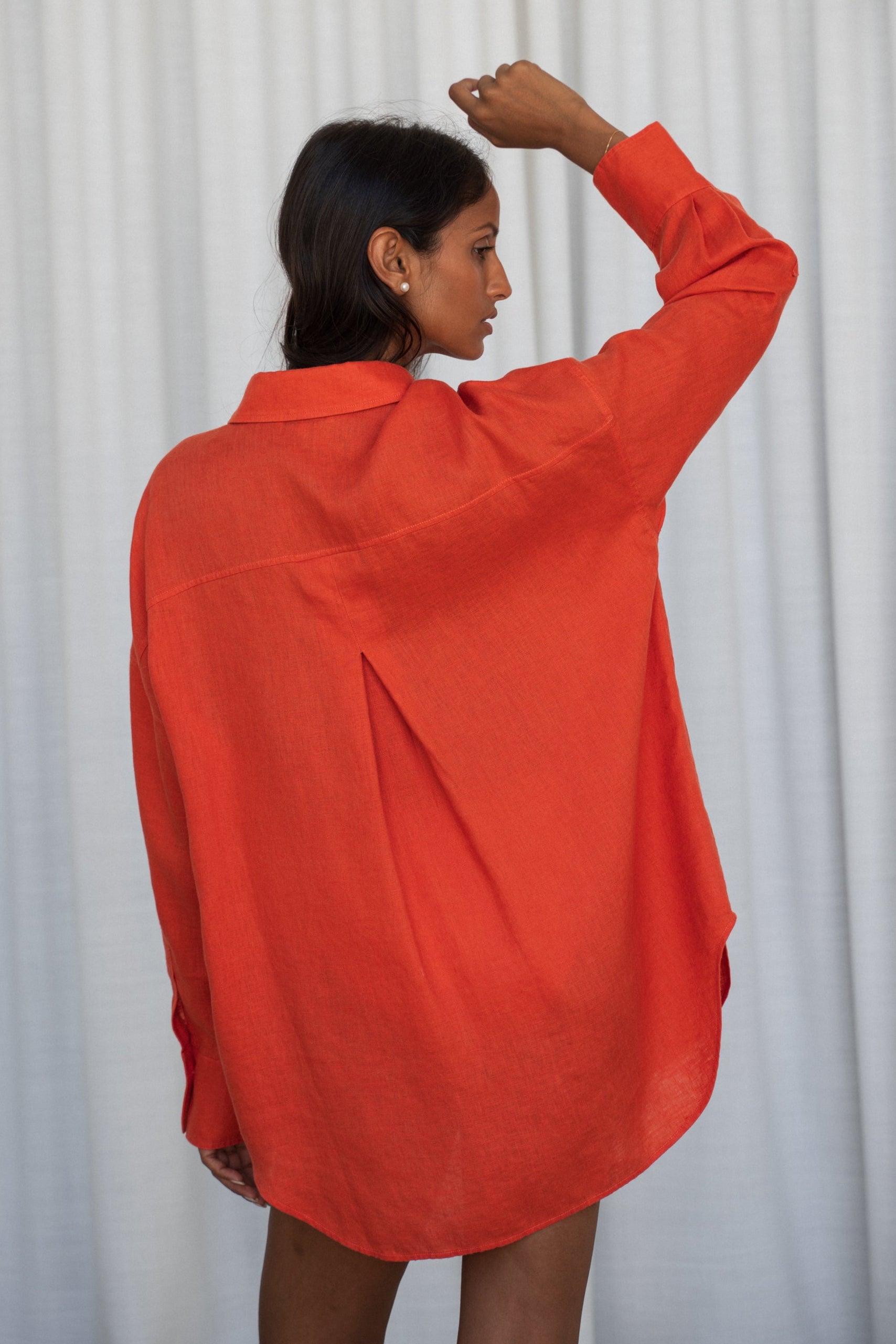 LILLY PILLY woman wearing a spritz Kirra linen shirt leaning against a  wooden wall while showing back view