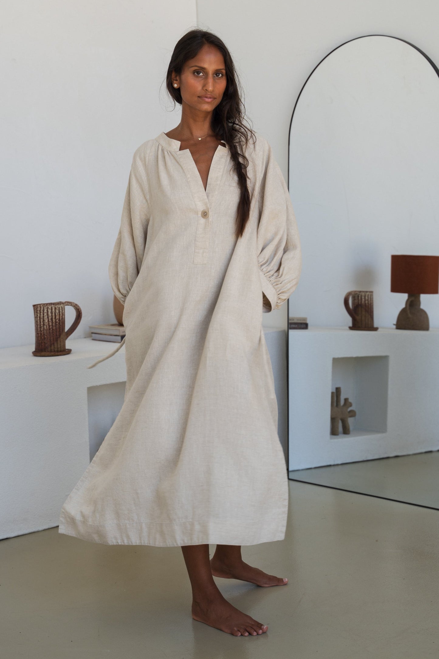 Woman wearing a Mae oatmeal linen dress twirling in a room with white walls and a mirror.
