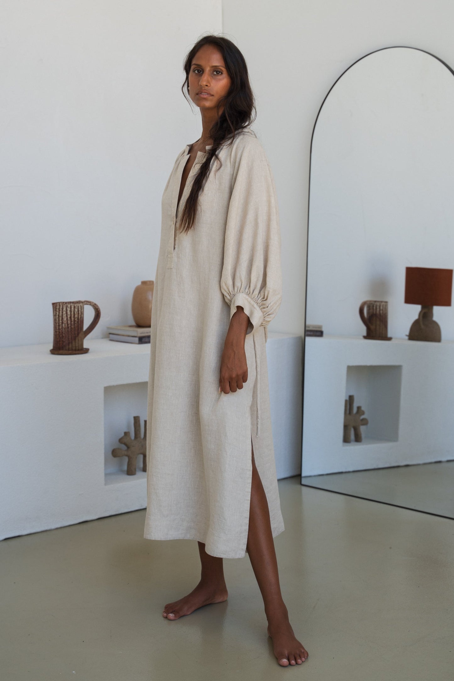 Woman wearing a Mae oatmeal linen dress close up view in a room with white walls and a mirror.