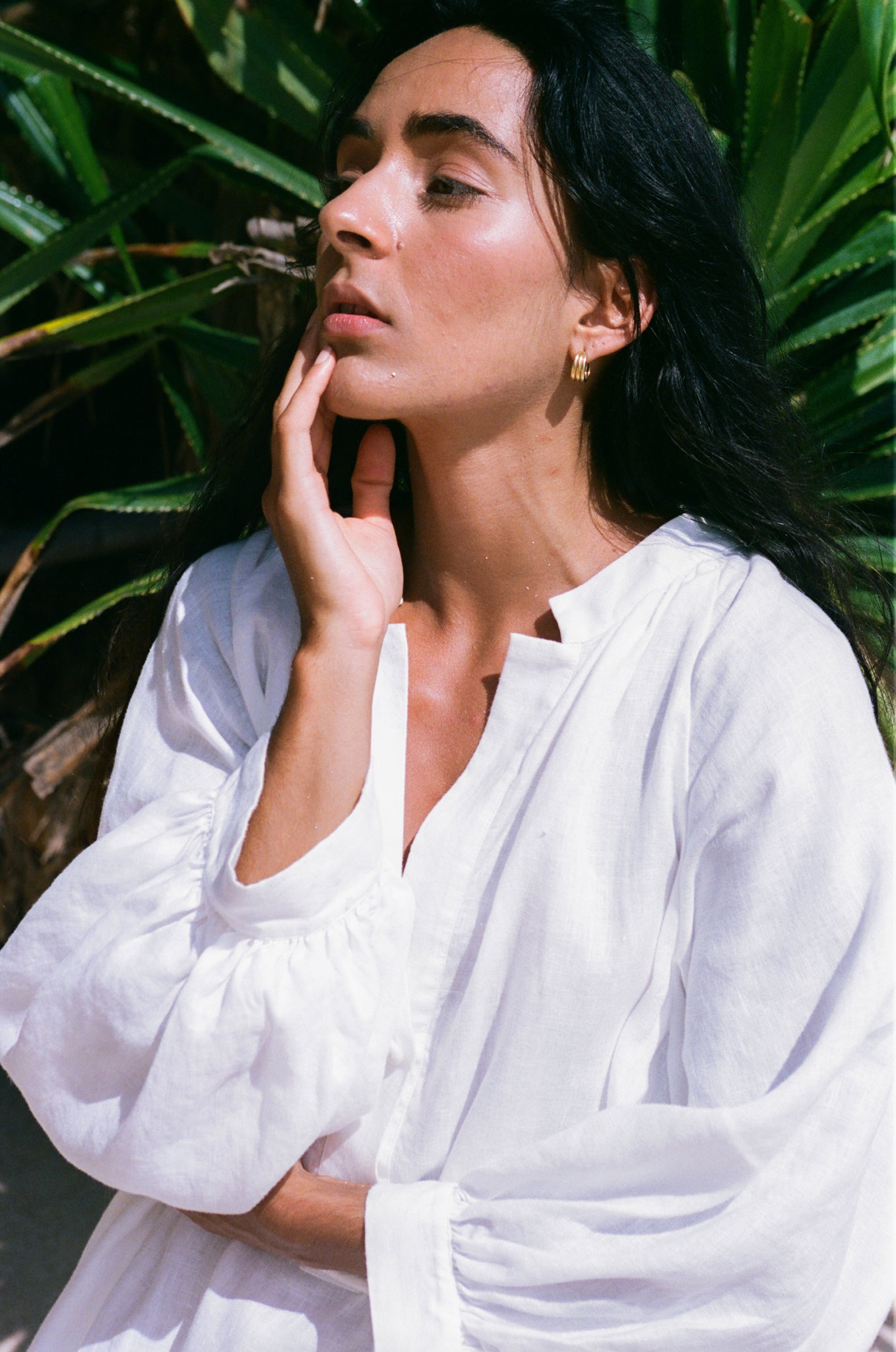 Woman in an ivory Mae linen dress standing in front of green plants