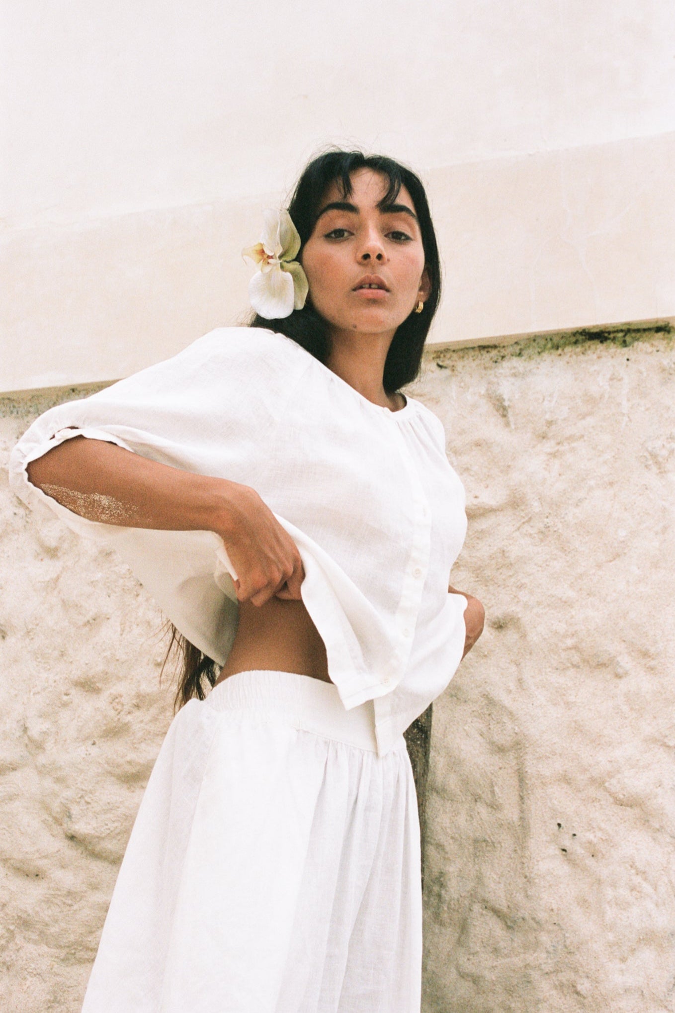 LILLY PILLY woman wearing an ivory Pia linen shirt top with ivory skirt standing by a textured wall