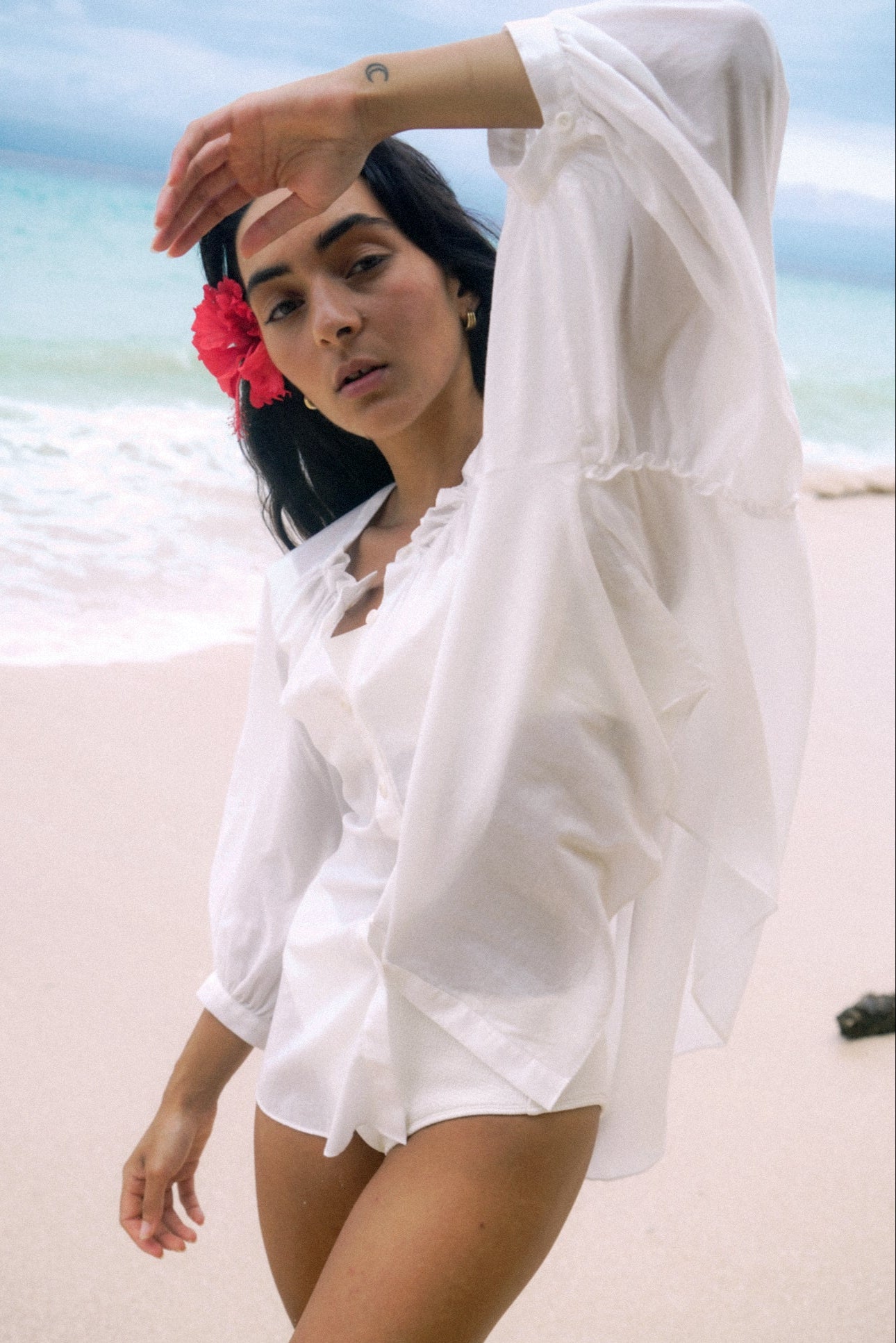 LILLY PILLY woman wearing a ivory Thalia cotton voile shirt blouse with a flower in her hair standing on the beach